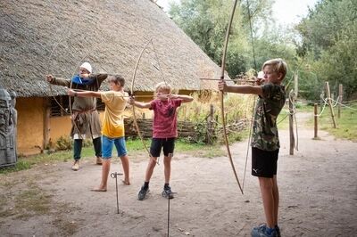 Drie jongens en een historische bewoner richten hun boog.