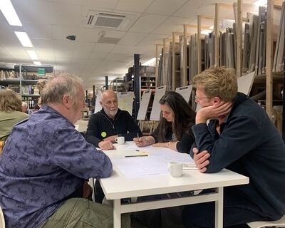 Groep mensen zit rond een tafel in een creatieve ruimte, verdiept in een discussiesessie met documenten en koffie.