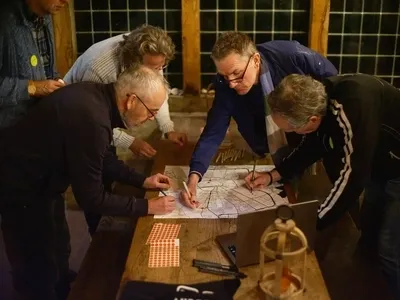 Vijf mensen verzamelen rond een tafel, terwijl ze aantekeningen maken op een grote kaart.