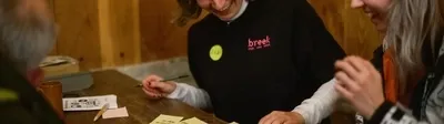 Een groep mensen aan een tafel die samen zijn en iets interactiefs doen, met lachende uitdrukkingen.