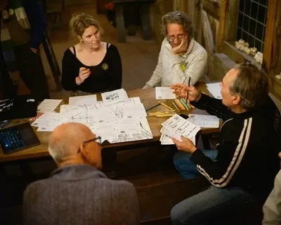 Groep mensen rond een tafel, die besprekingen voeren en aantekeningen bekijken, terwijl een laptop aan de zijkant staat.