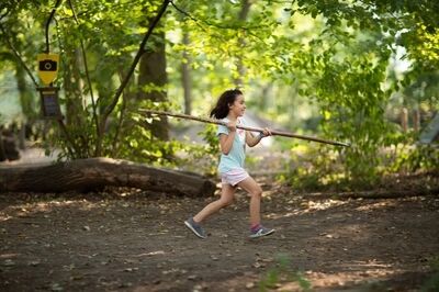 Lachend meisje werpt speer in het bos