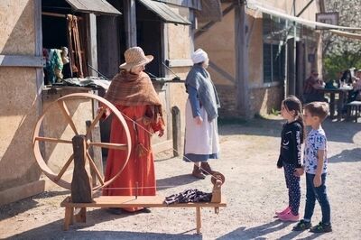 Kinderen observeren demonstratie van traditionele ambachten bij een middeleeuws evenement. Een vrouw spin met een spinnenwiel.